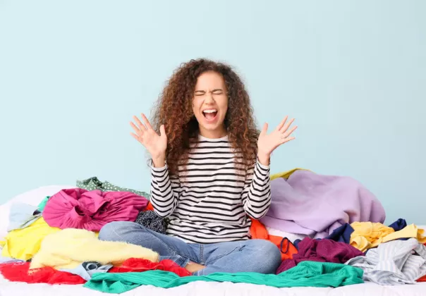 Woman sitting on a bed with a pile of clothes around her